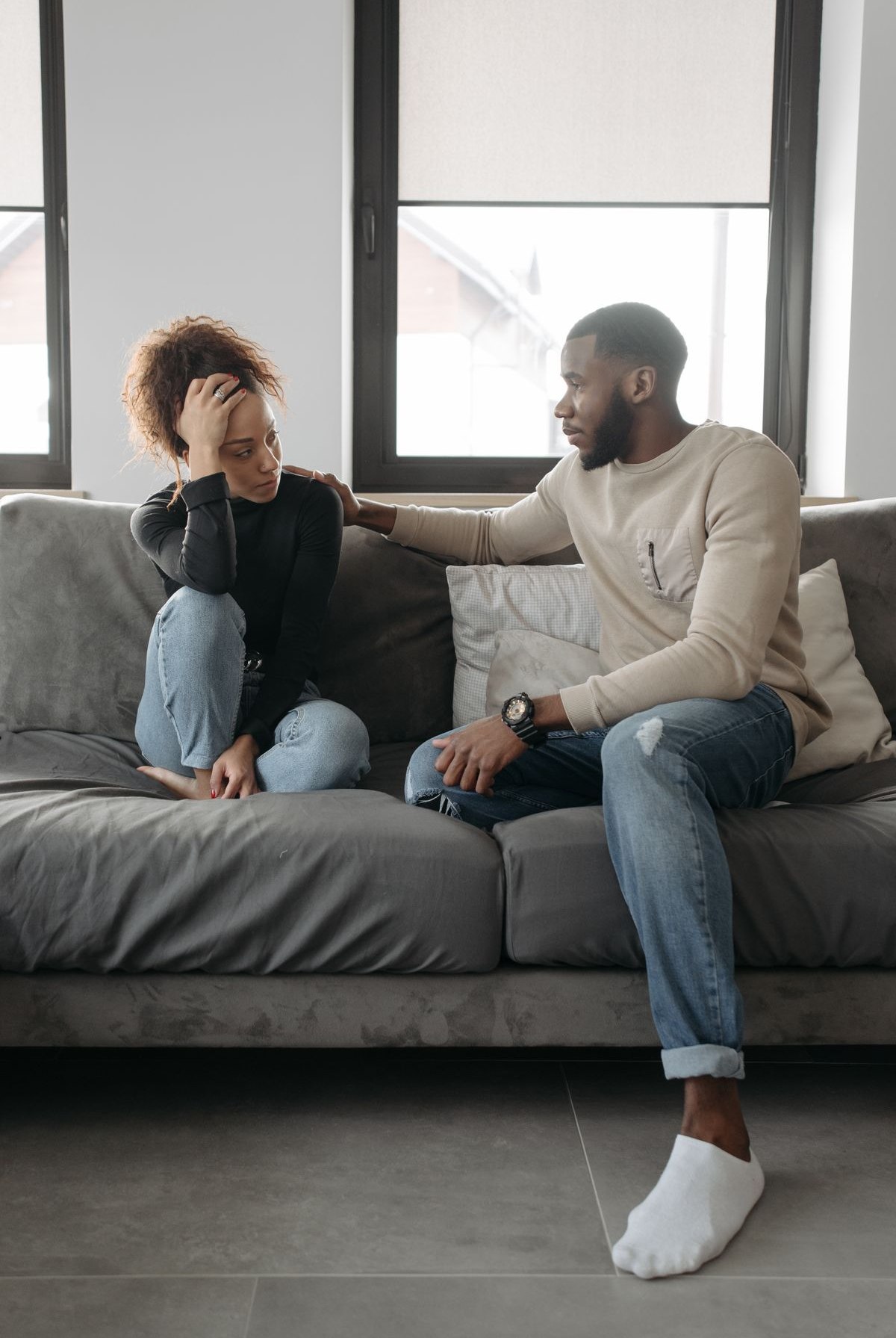 A couple on a sofa, one reaching out to comfort the other, representing repair after an affair