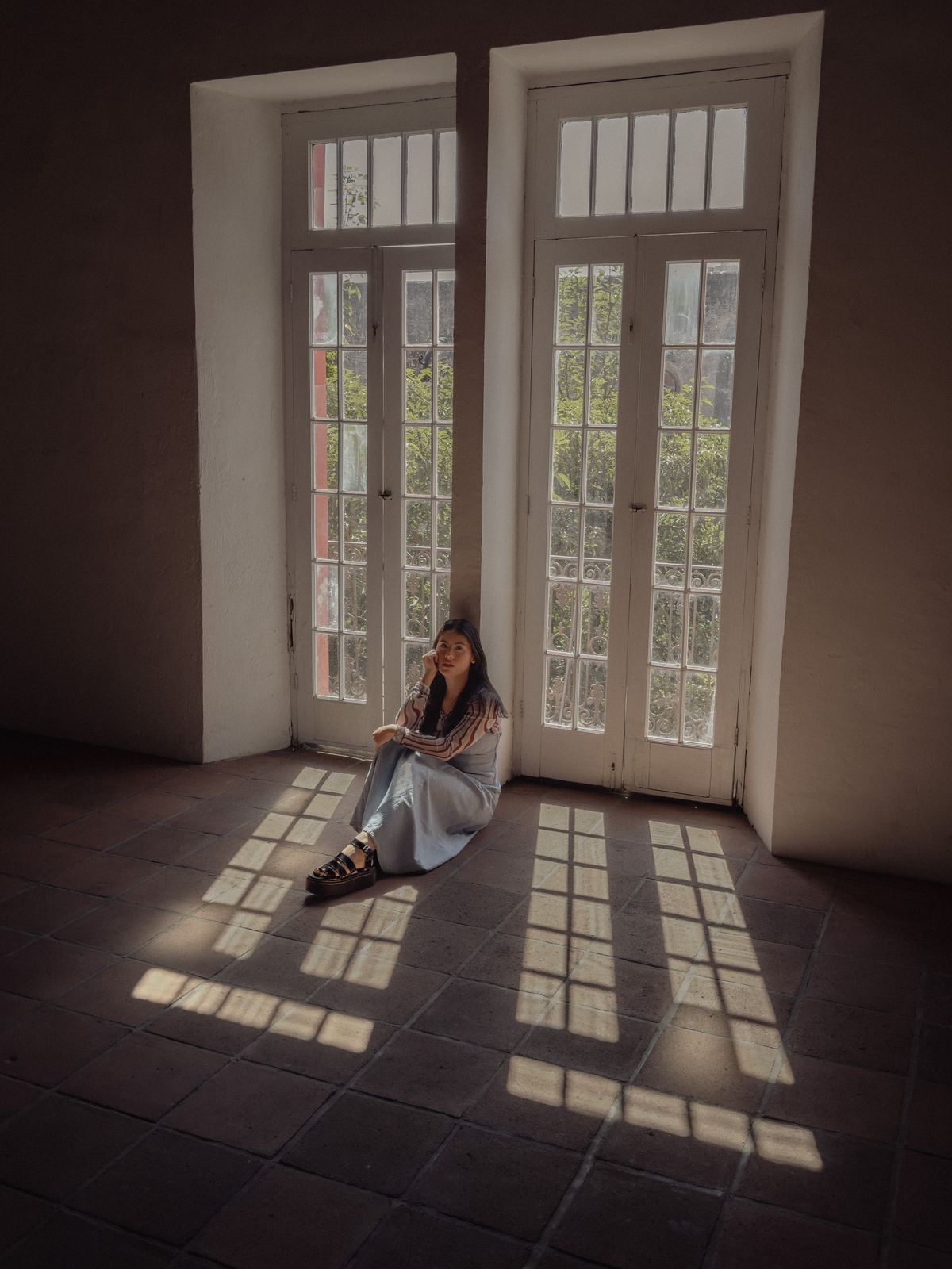 A woman sitting calmly in light from tall windows, representing space and steadiness after a controlling relationship