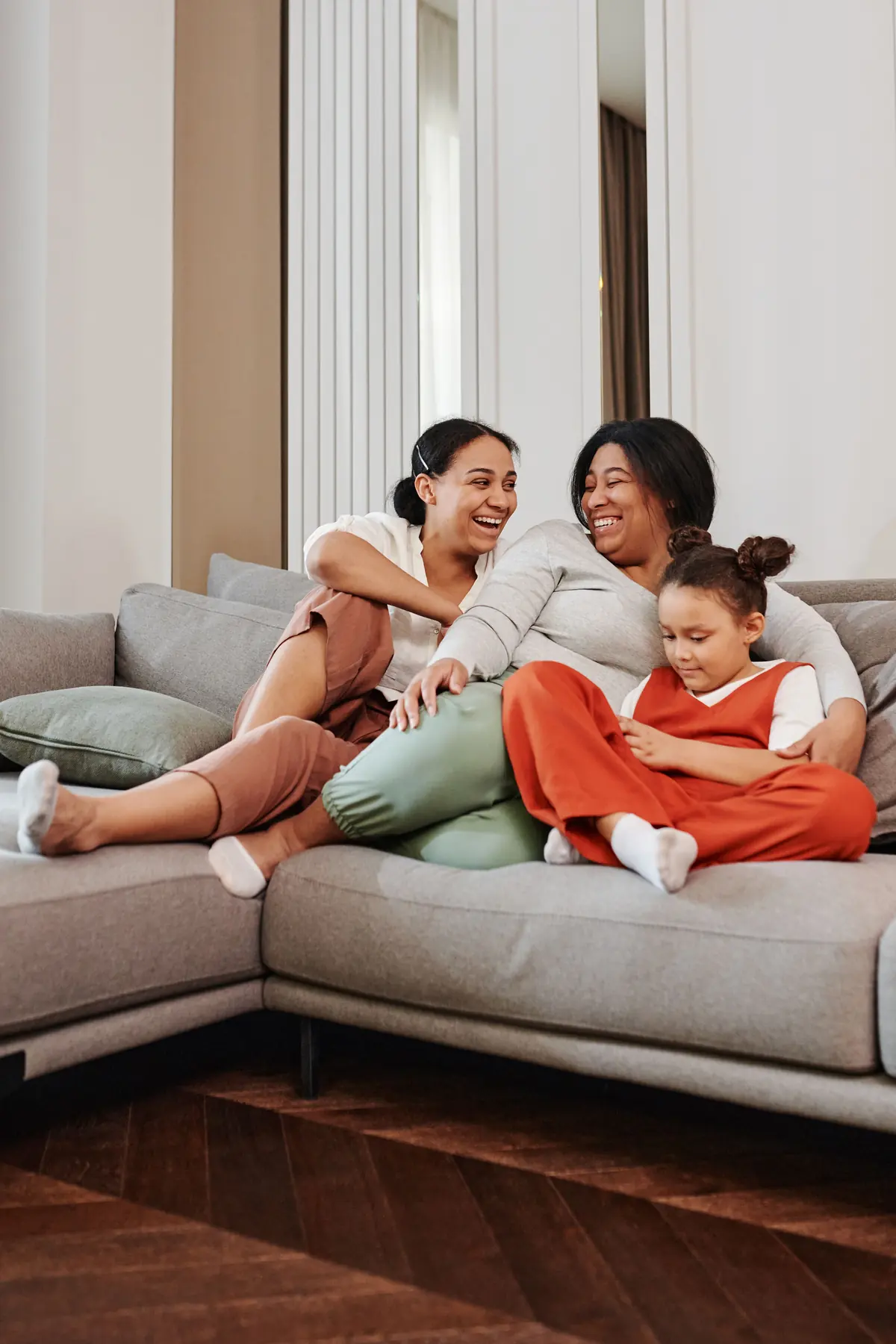 A mother laughing with her teenage daughter and younger child on the sofa at home