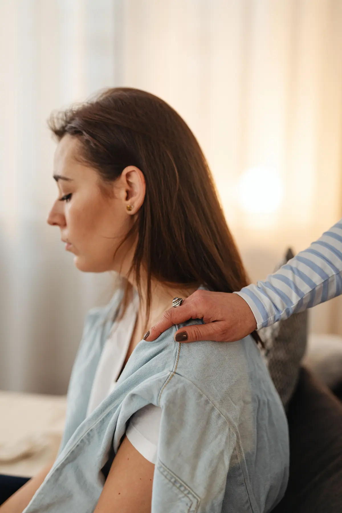 A woman sitting quietly while another person rests a hand on her shoulder