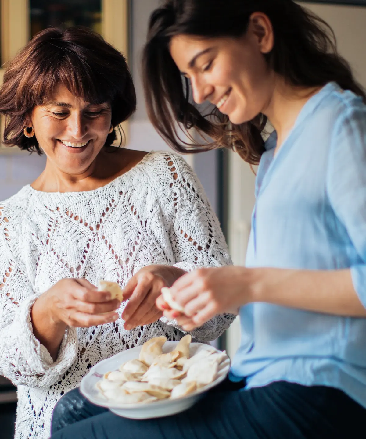 Two women laughing while preparing food together in a kitchen