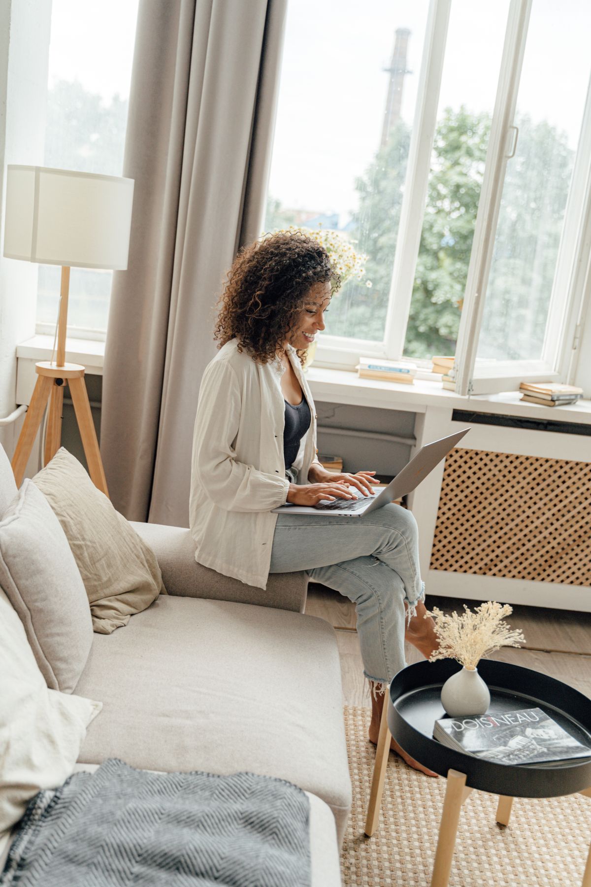 A person sitting on a sofa at home with a laptop, in soft daylight by a window