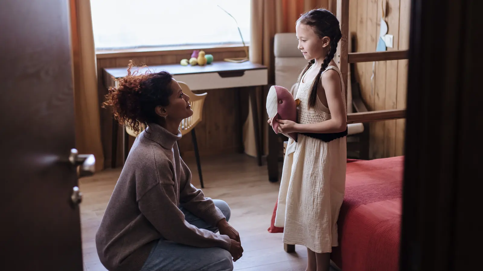 A parent crouching down to talk with her young daughter at eye level