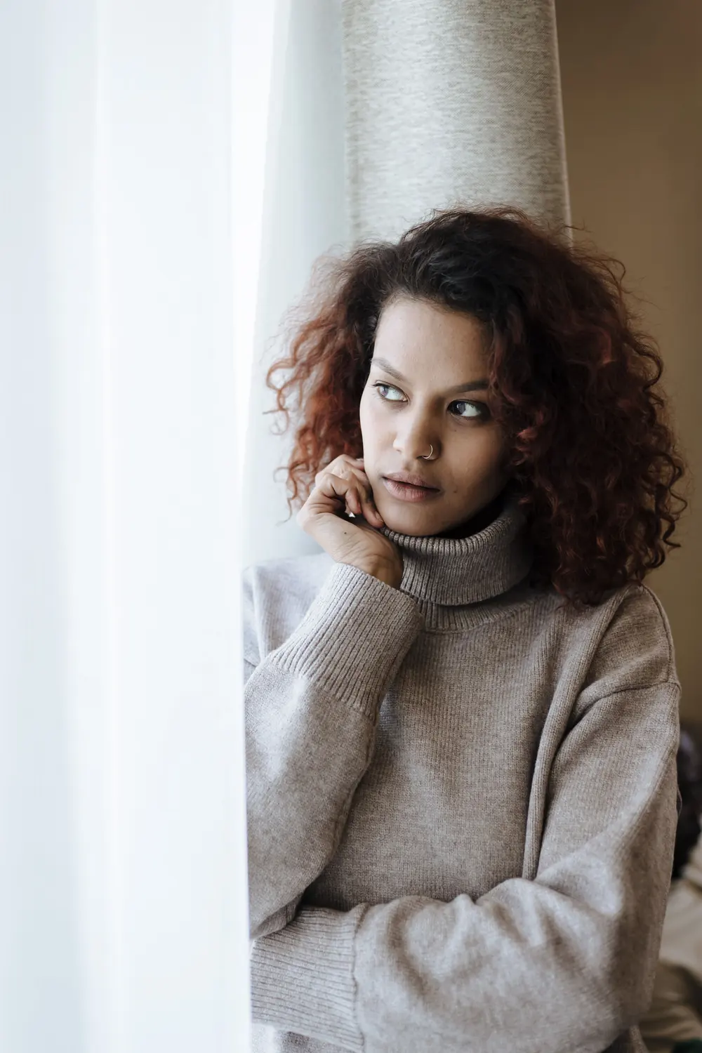 A woman thinking, resting her chin on her hand in soft daylight