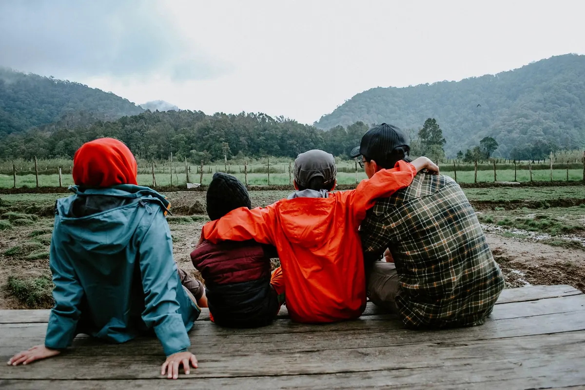 Four people sit close outdoors, arms around each other, looking at the hills