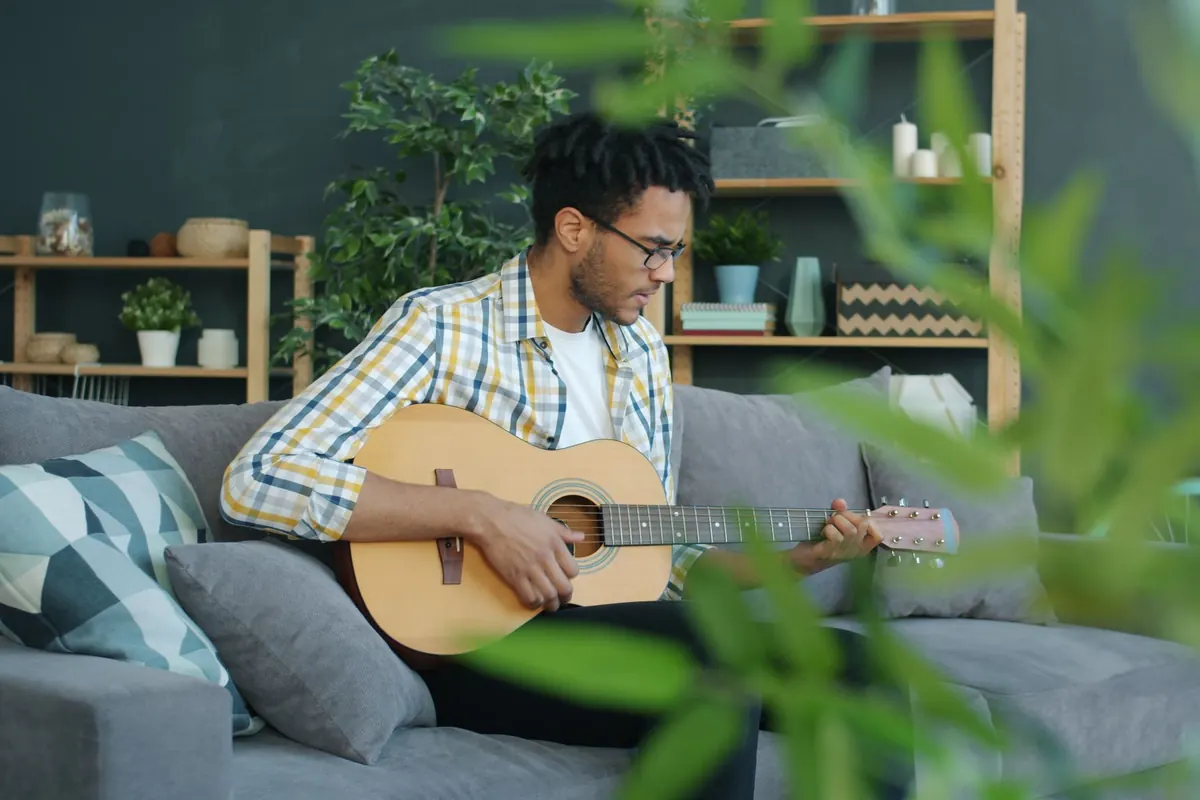 A young man plays an acoustic guitar on a sofa at home