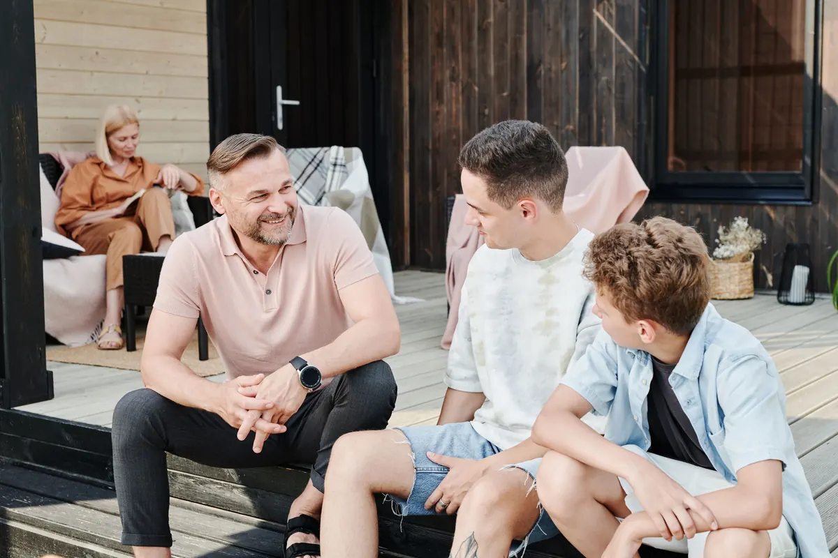 A father chats with his two teenage sons on the porch steps