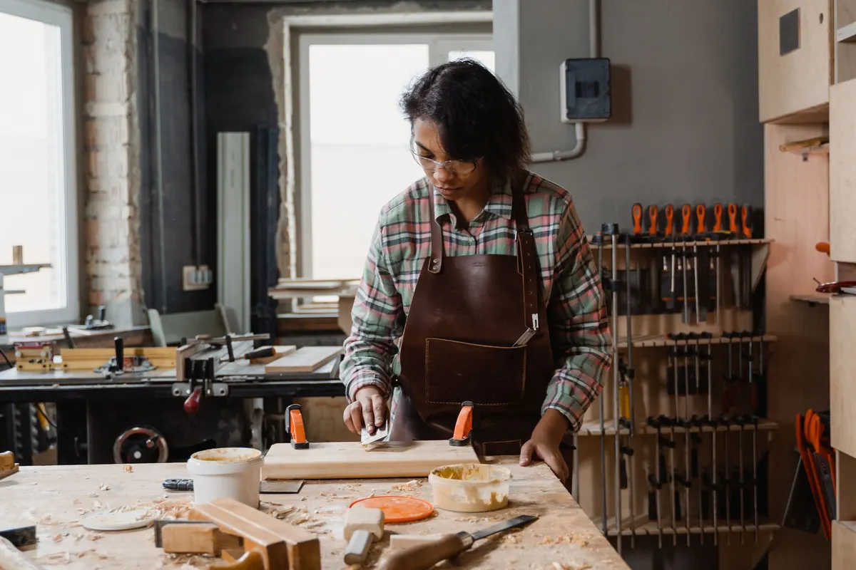 A woman in a leather apron works at a bench in a carpentry workshop