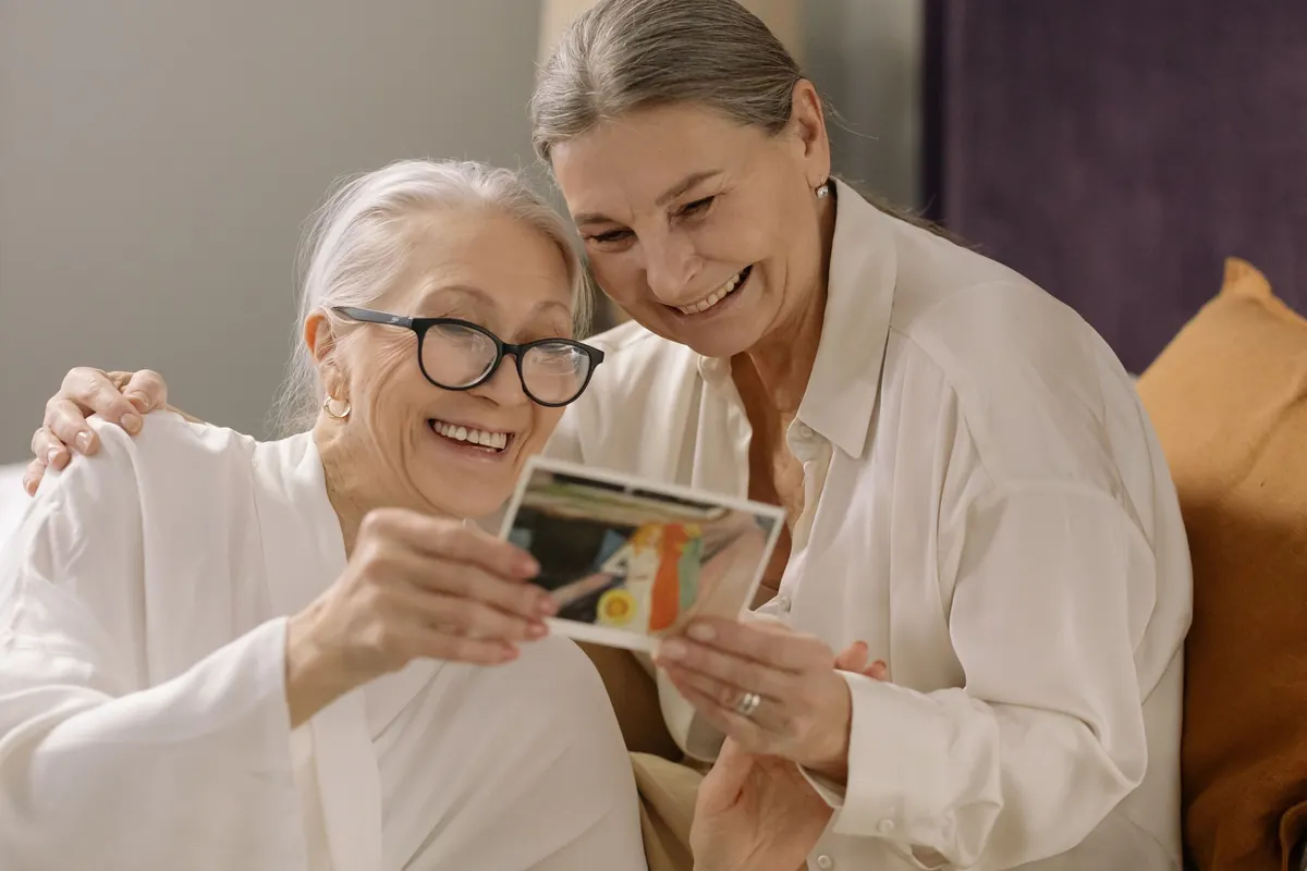 Two older women smile as they look at a photograph together