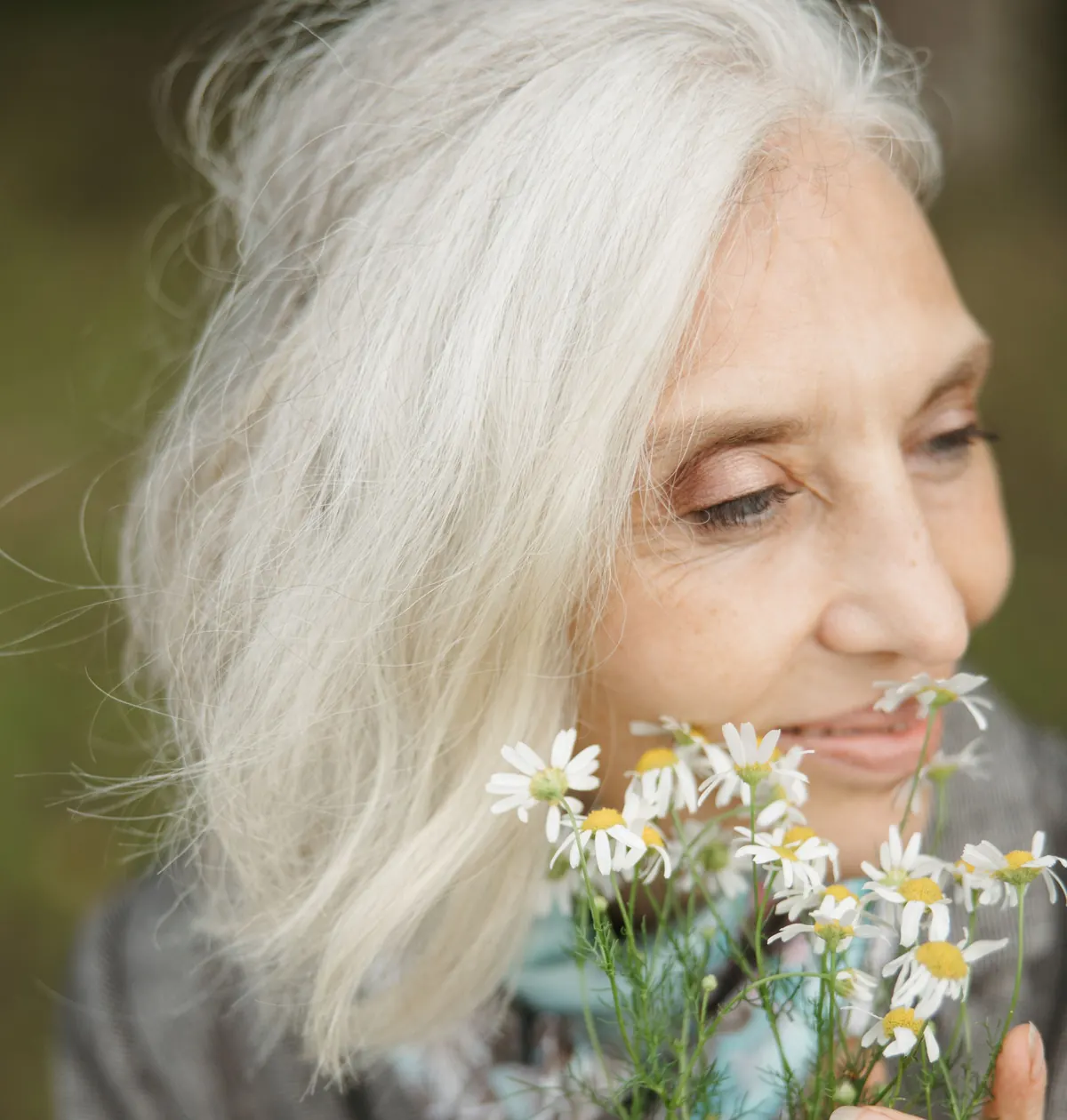 An older woman with white hair smiles softly as she holds a small bunch of daisies