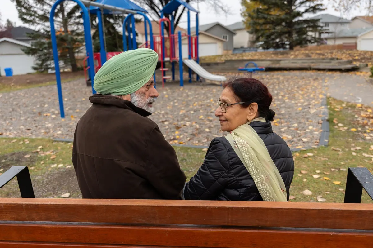 An older couple on a park bench in autumn, turned toward each other