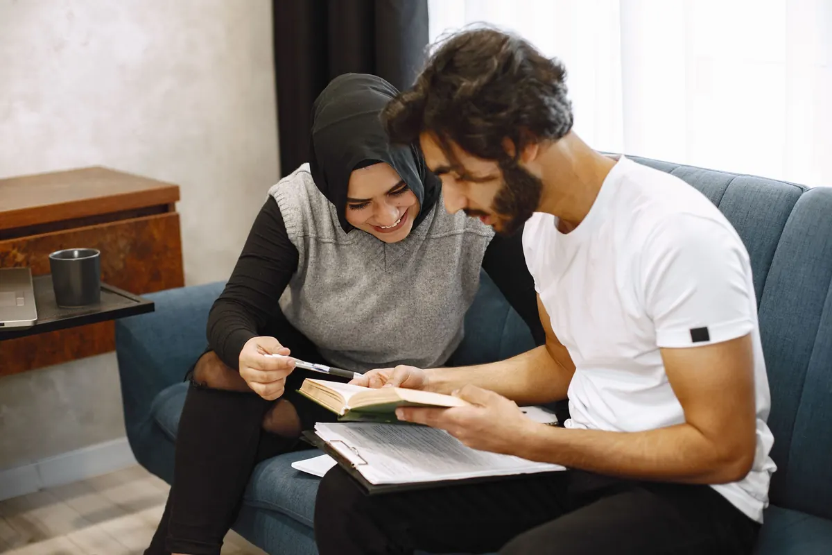 A young couple sit close on a sofa, making notes in a notebook