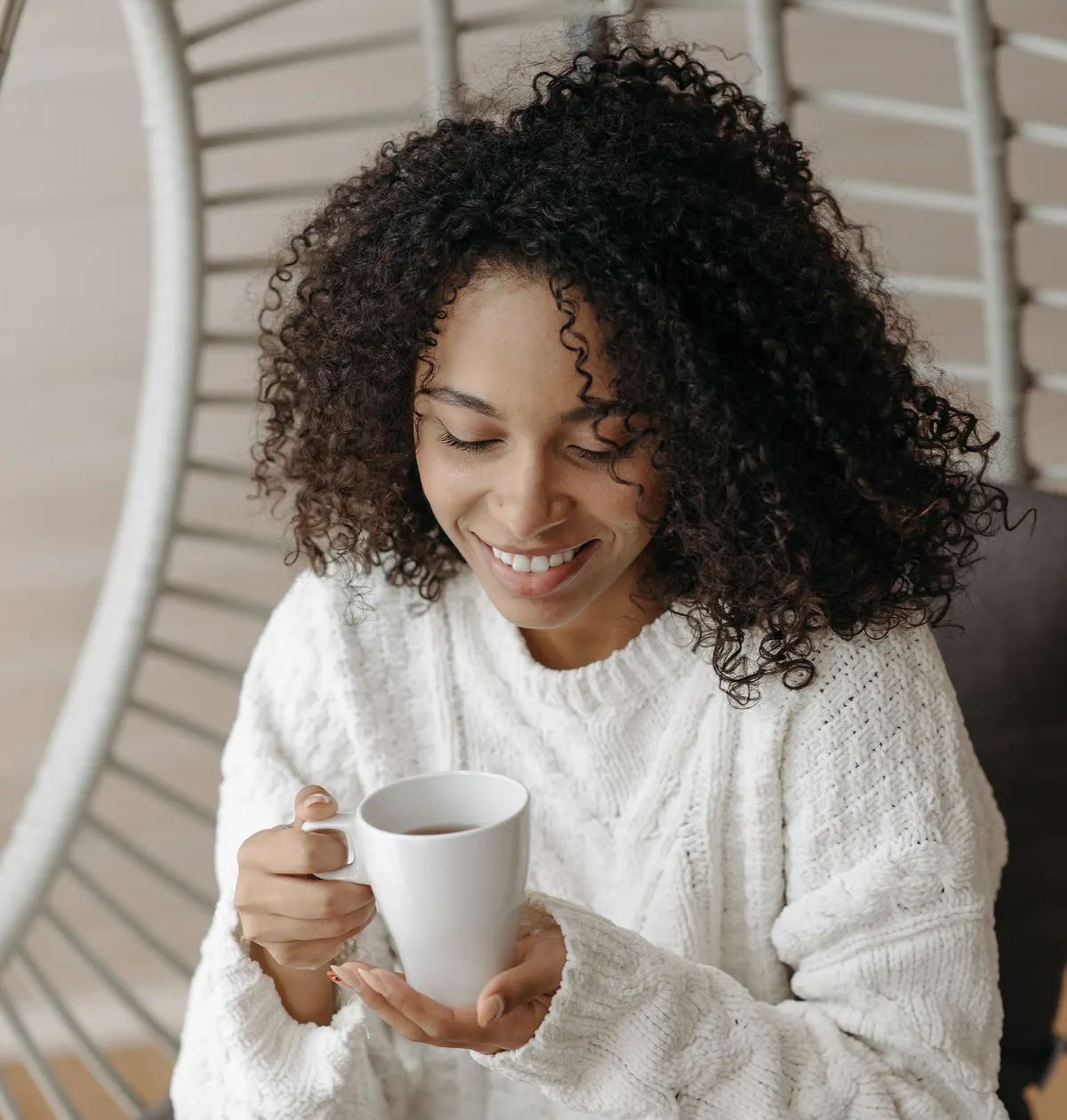 A woman with curly hair smiles down at the mug of tea in her hands
