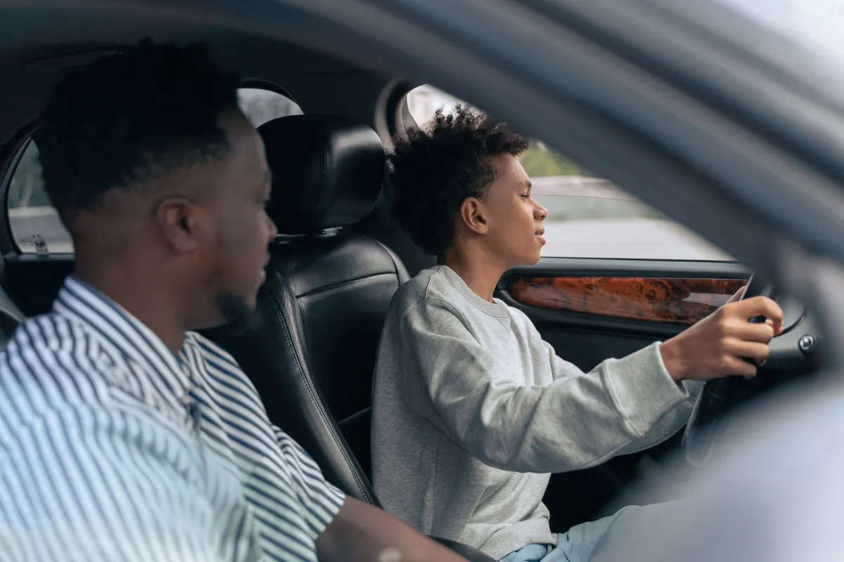A father sits beside his teenage son as the teen practises driving