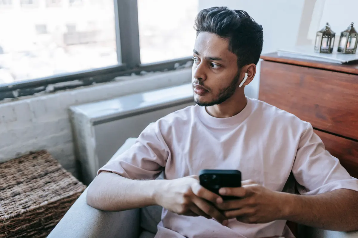 A young man holding his phone and looking away, thinking over a message